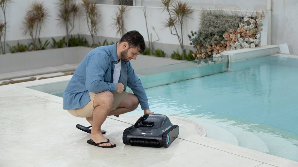 A man prepares to place the Aiper pool cleaner into a modern backyard swimming pool.