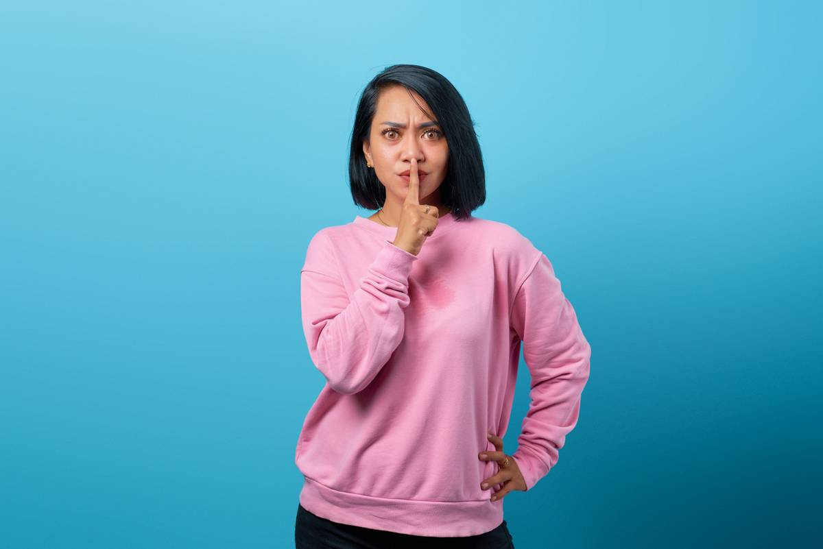 a woman in a pink sweater making a hush gesture