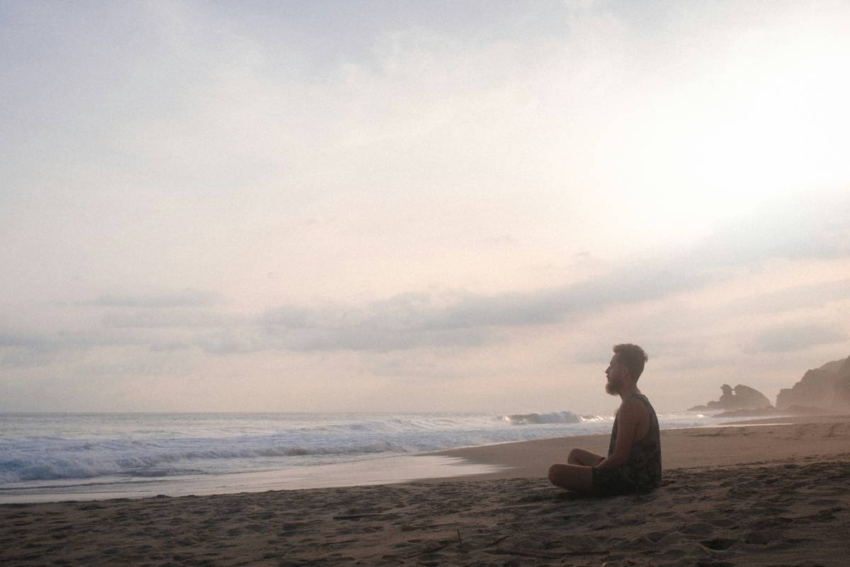 guy sits cross-legged on the beach and meditates, the wide sea in the background